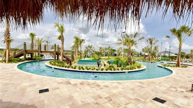 A pool area with palm trees, a bridge, and a tiled walkway.
