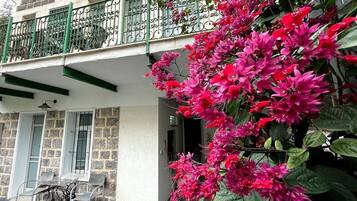 A balcony with a wrought iron railing, a stone wall, and a table with chairs.