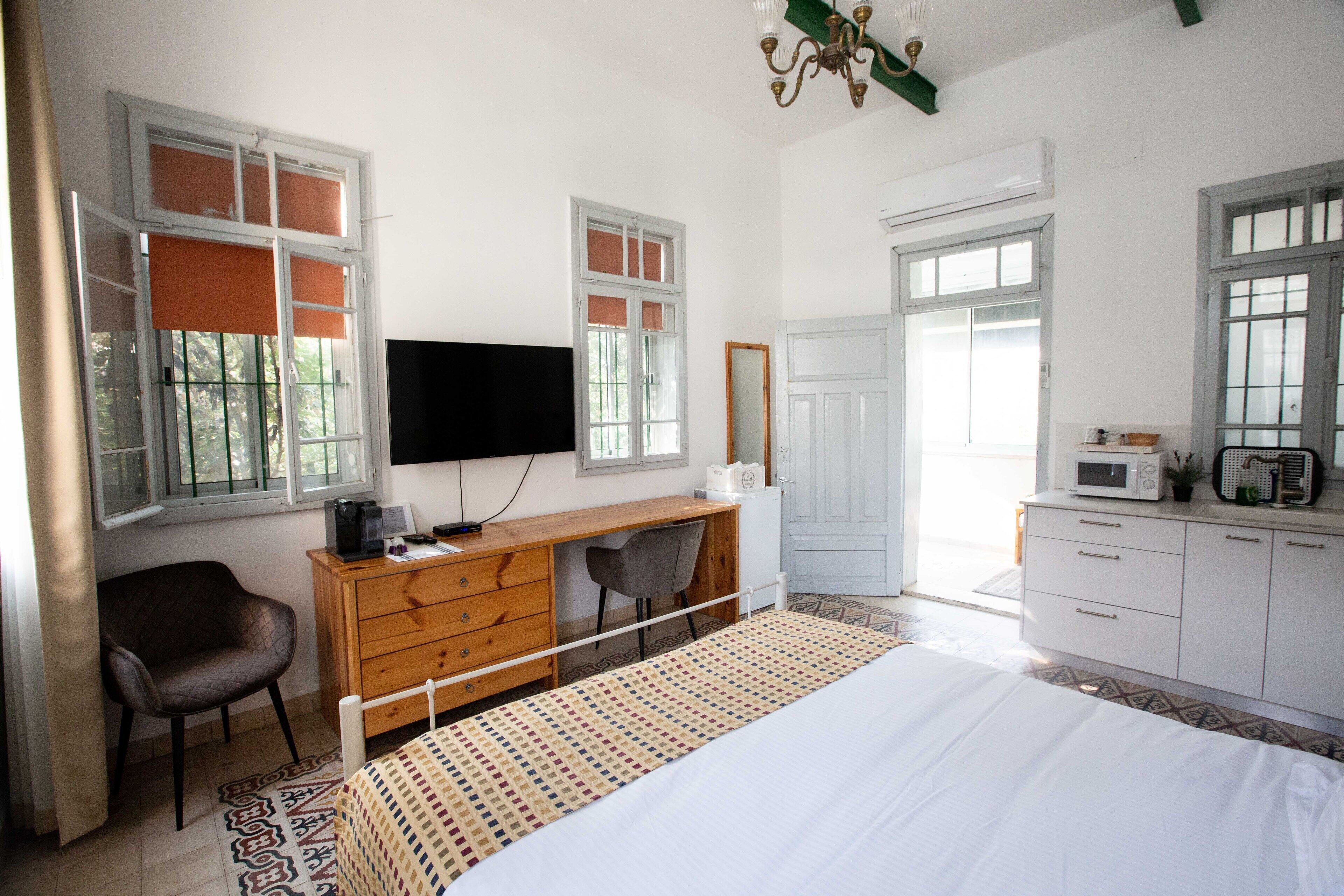 Un dormitorio con cama, escritorio, silla, televisor y kitchenette.