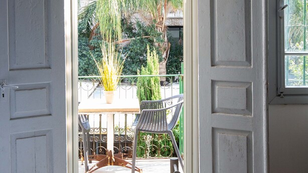 Une pièce avec un lit, une table entourée de chaises et une vue sur un jardin, visible à travers une porte ouverte.