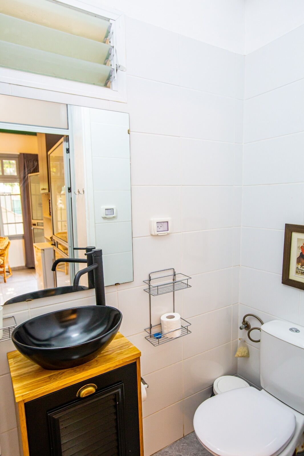 A compact bathroom with a black sink, a toilet, and a mirror.