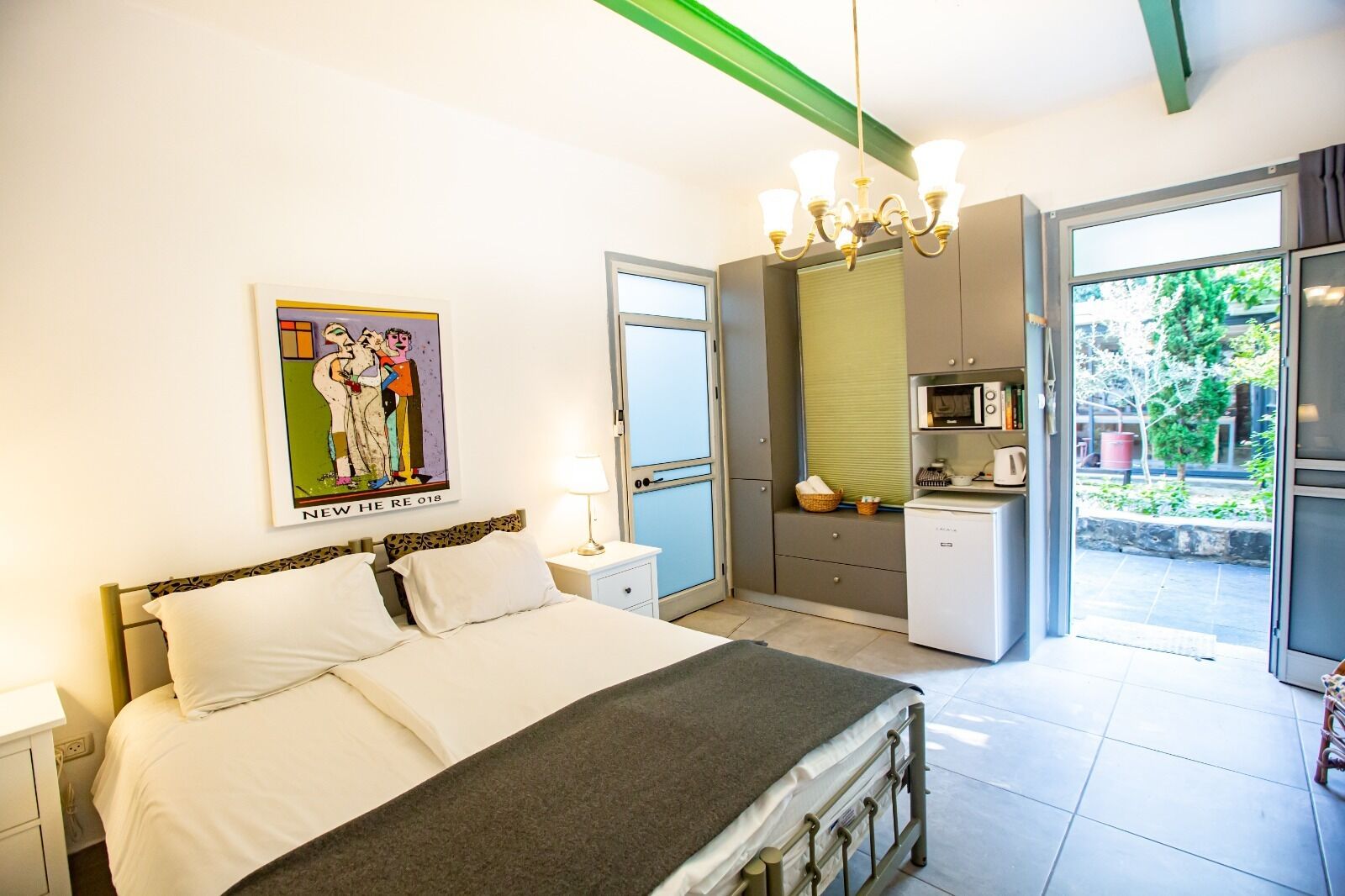 Un dormitorio con una cama, una mesita de noche y un cuadro. Cuenta con una kitchenette con microondas y una ventana.
