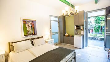 Un dormitorio con una cama, una mesita de noche y un cuadro. Cuenta con una kitchenette con microondas y una ventana.