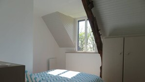 A bedroom with a sloped ceiling, a window, a bed with patterned bedding, and a wardrobe.
