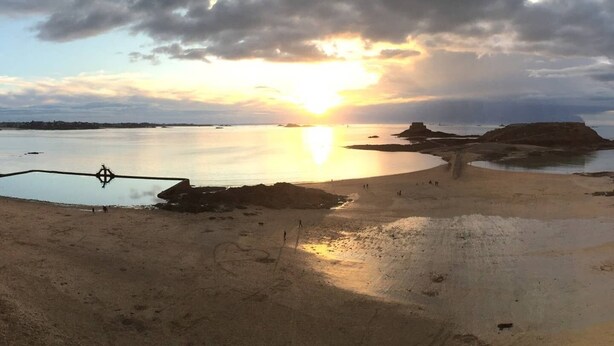 A beach with a calm sea, a sunset, and a compass in the foreground.
