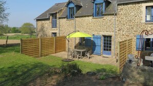 A stone house with a patio, a table with chairs, and a yellow umbrella.