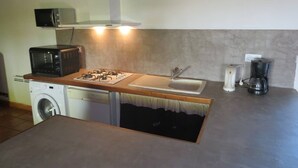 A compact kitchen with a built-in washing machine, a microwave, a gas stove, and a coffee maker.