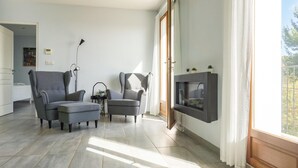 A modern living room with two grey armchairs, a small ottoman, a floor lamp, and a TV mounted on the wall.