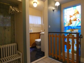 Ein Badezimmer mit Holzboden, Toilette in Weiß und einem Buntglasfenster.