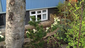 Een woongebouw met een blauwe gevel, een zichtbaar raam en een tuin met planten en een boom.