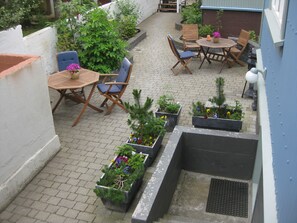 Ein Terrassenbereich mit Pflasterboden, Holzmöbeln und Topfpflanzen.