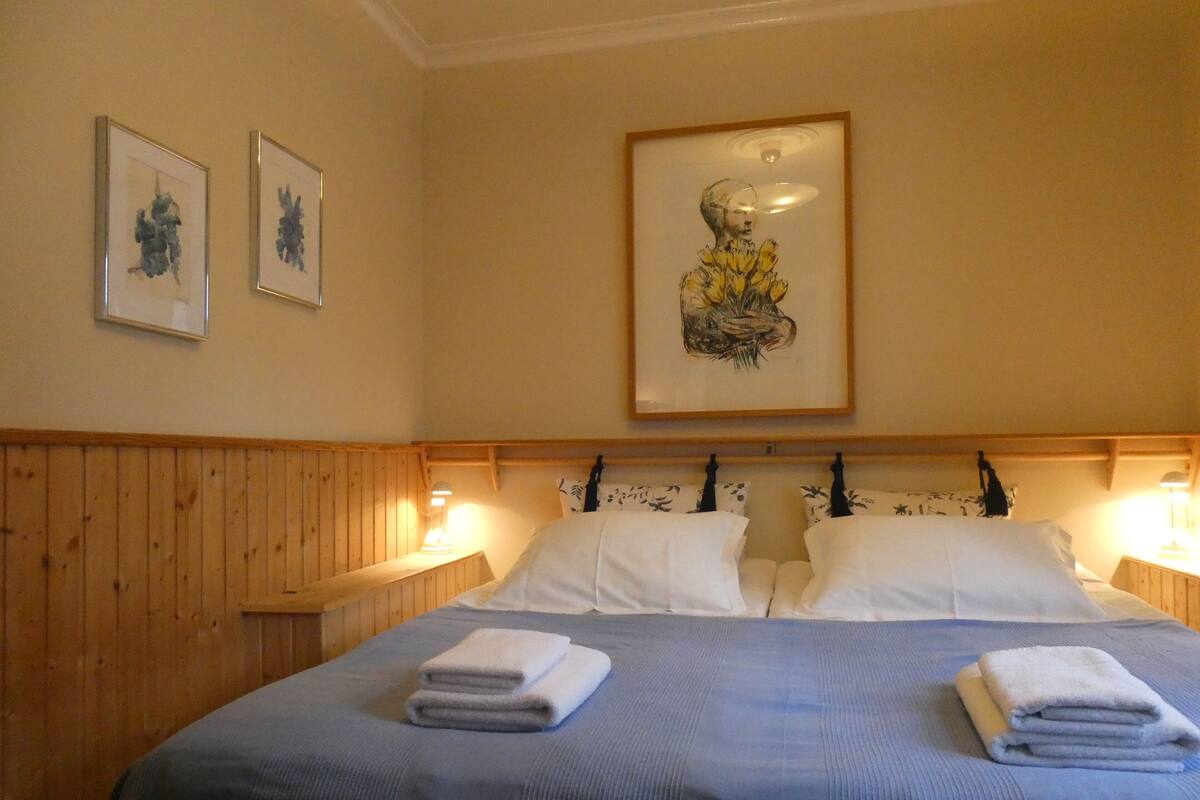 Une chambre d’hôtel avec une tête de lit en bois, deux lits avec du linge de lit blanc et des œuvres d’art encadrées accrochées au mur.
