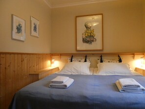 Ein Hotelzimmer mit einem hölzernen Kopfteil, zwei Betten mit weißer Bettwäsche und gerahmten Kunstwerken an der Wand.