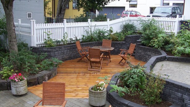 Een terras met houten meubels, een witte schutting en planten in potten.