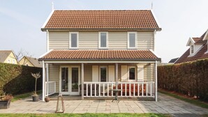 A two-story house with a tiled roof, a covered porch with a railing, and a paved driveway. - 3 bedroom stunning home in Wemeldinge (Wemeldinge)