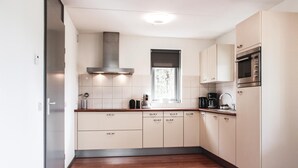 A modern kitchen with white cabinets, a stainless steel range hood, a window, and a microwave. - 3 bedroom stunning home in Wemeldinge (Wemeldinge)