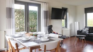 A modern living room with a dining area, large windows, a flat-screen TV, and a black leather sofa. - 3 bedroom stunning home in Wemeldinge (Wemeldinge)