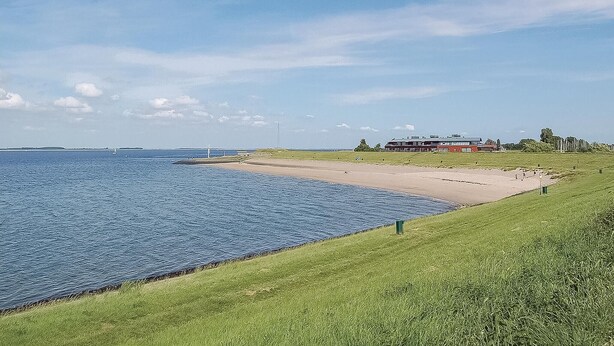 A coastal landscape with a sandy beach, grassy areas, and a large building with a red roof. - 3 bedroom stunning home in Wemeldinge (Wemeldinge)