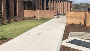 Un edificio moderno con fachada de ladrillo, un camino de hormigón y una pequeña zona ajardinada.