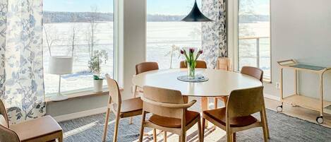A dining area with a round table, six chairs, a vase with flowers, and a pendant light.
