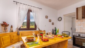 A cozy kitchen with a wooden table set for dining, a window with curtains, a clock on the wall, and a stove.