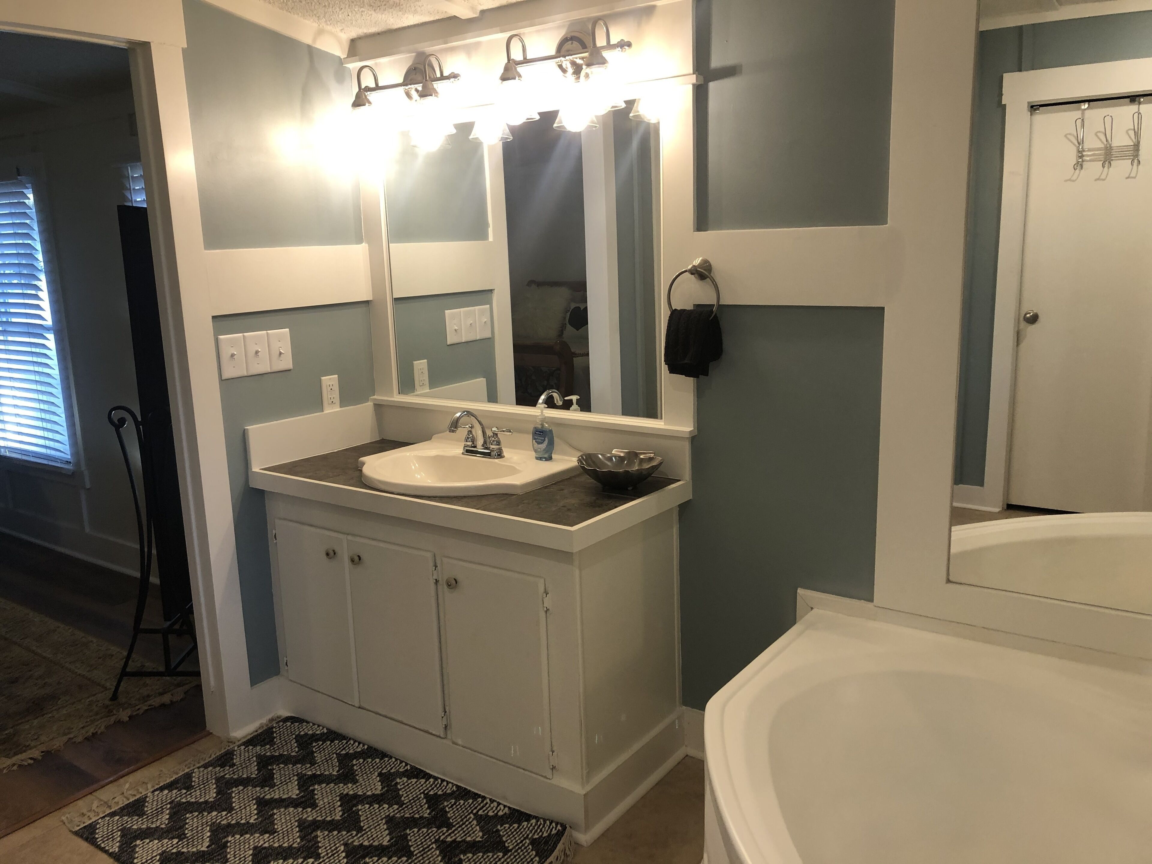 Un baño con lavamanos blanco, un espejo grande y una bañera.