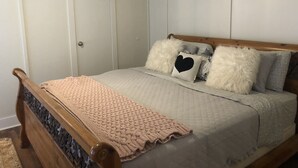 Un dormitorio con estructura de cama de madera, cubrecama acolchado y varias almohadas, incluyendo una con diseño de corazón.