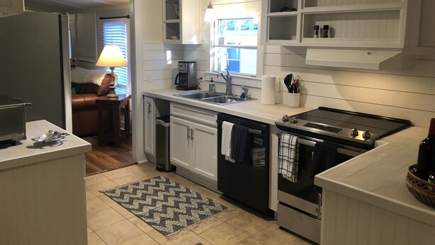Una cocina compacta con armarios blancos, horno empotrado, cafetera y lavabo.