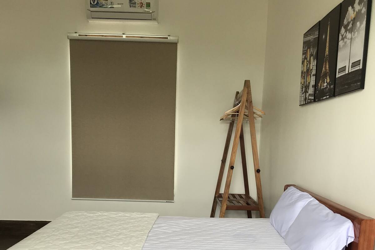A bedroom with a wooden bed, a wooden ladder, a white mattress, and a wall-mounted air conditioner.