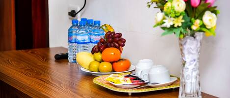 Una mesa de madera con un frutero, botellas de agua, un florero y una bandeja con tazas y un paquete.
