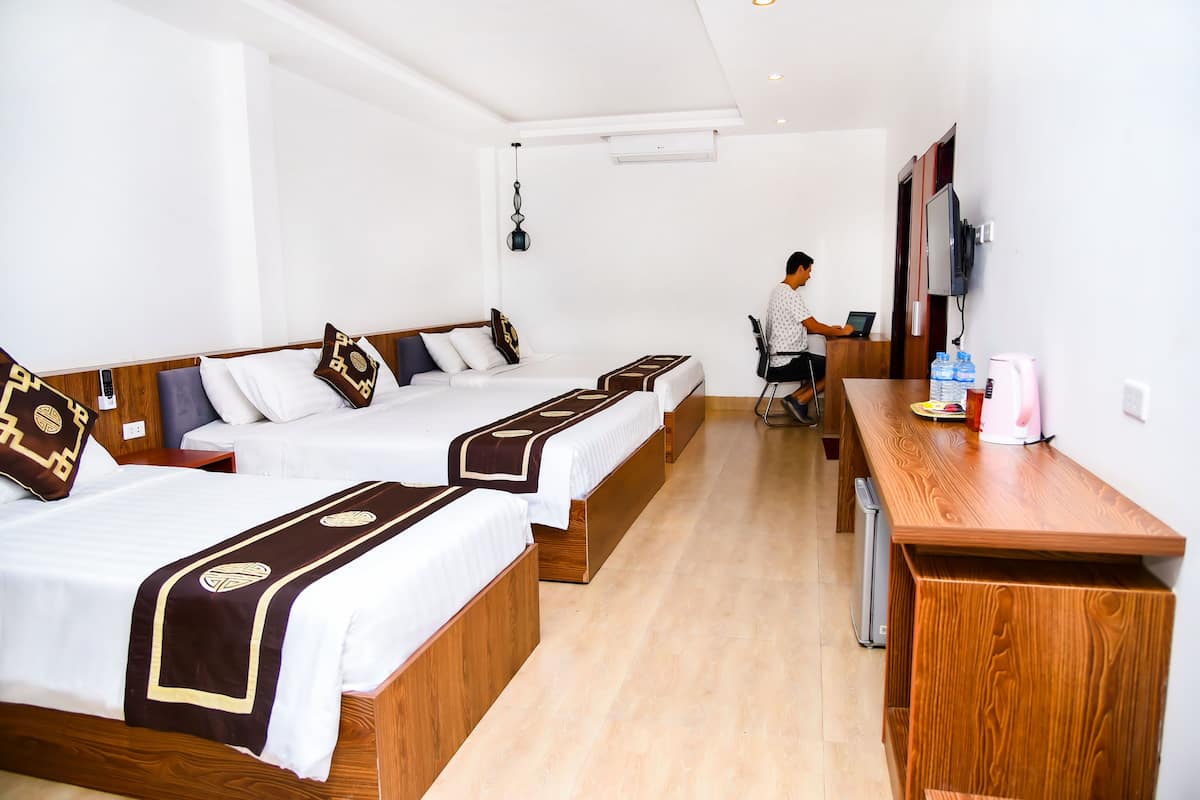 Quarto de hotel com três camas de madeira, uma escrivaninha e uma televisão.