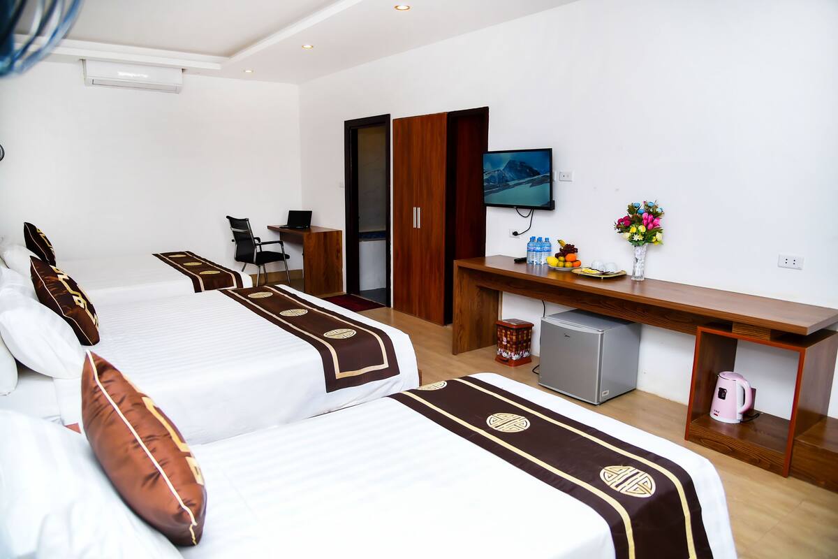 Quarto de hotel com duas camas, uma escrivaninha, televisão, mini-geladeira e cafeteira.