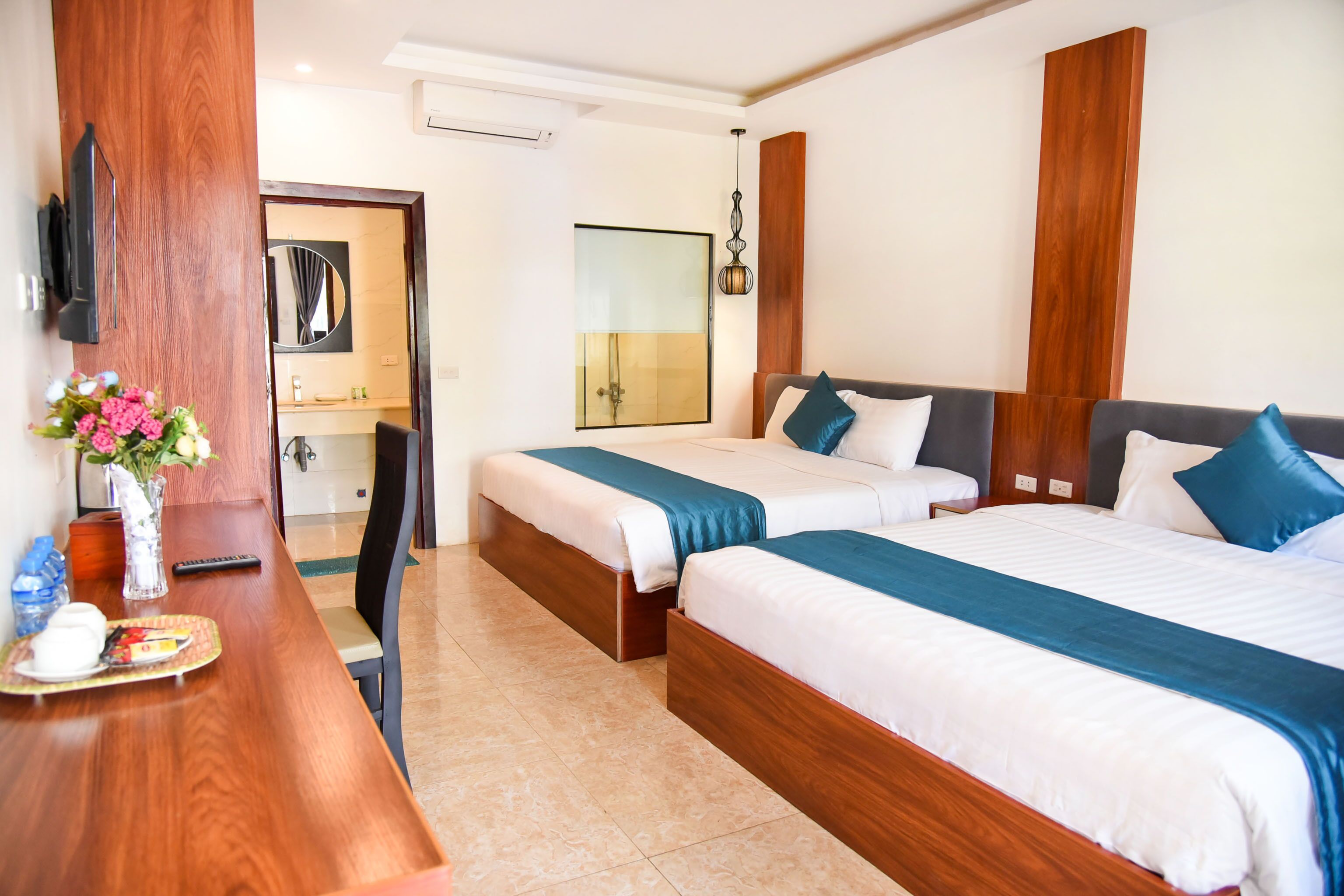 A hotel room with two beds, a wooden desk, a mirror, and a TV.