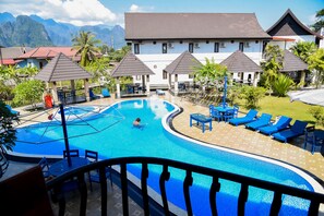 A swimming pool with lounge chairs and umbrellas, surrounded by a building with multiple roofs and a view of mountains. - Diamond Resort Vang Vieng (Vang Vieng)