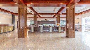 A spacious lobby with a central reception desk, wooden pillars, and a modern ceiling design.