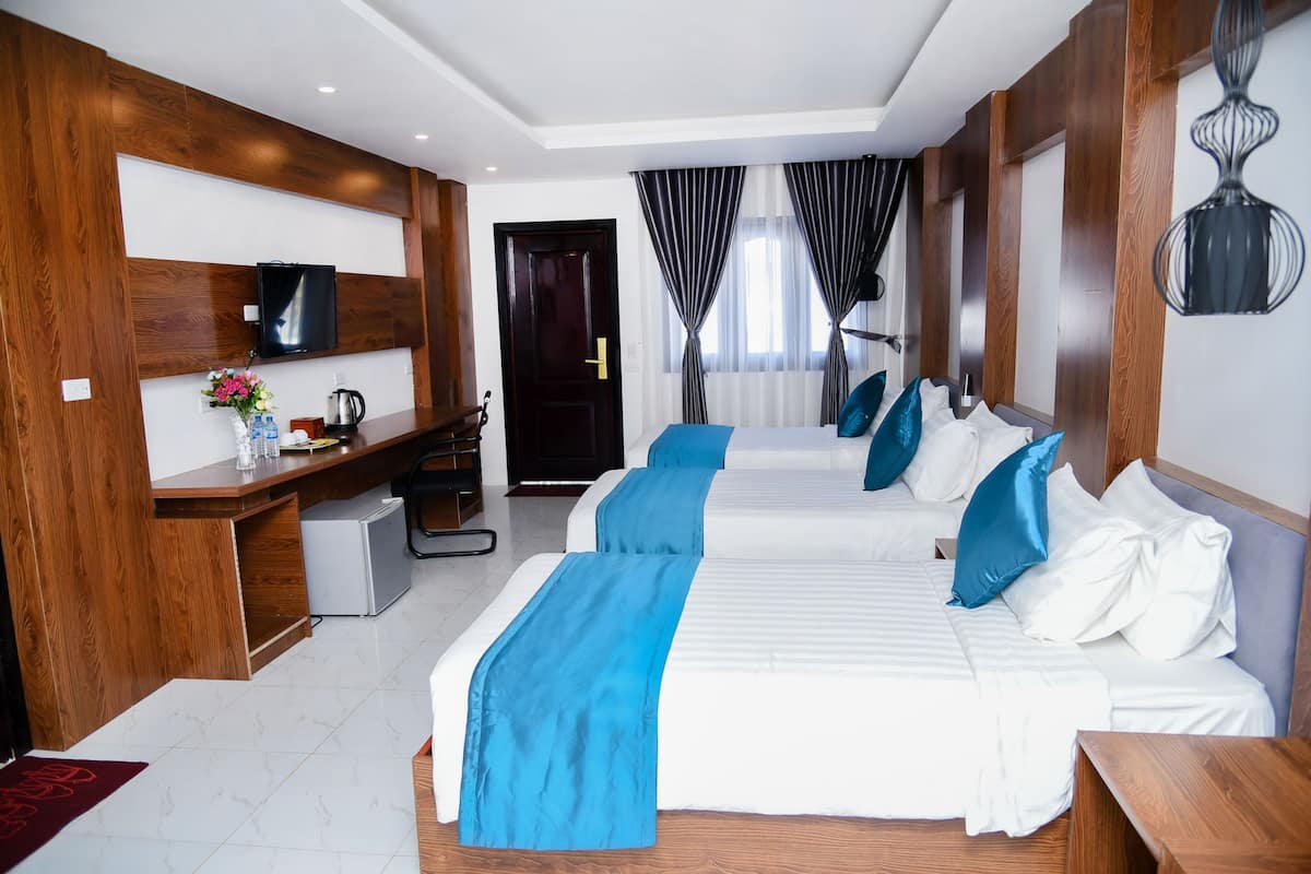 Quarto de hotel com duas camas, uma mesa de escritório com computador, televisão e janela com cortinas.