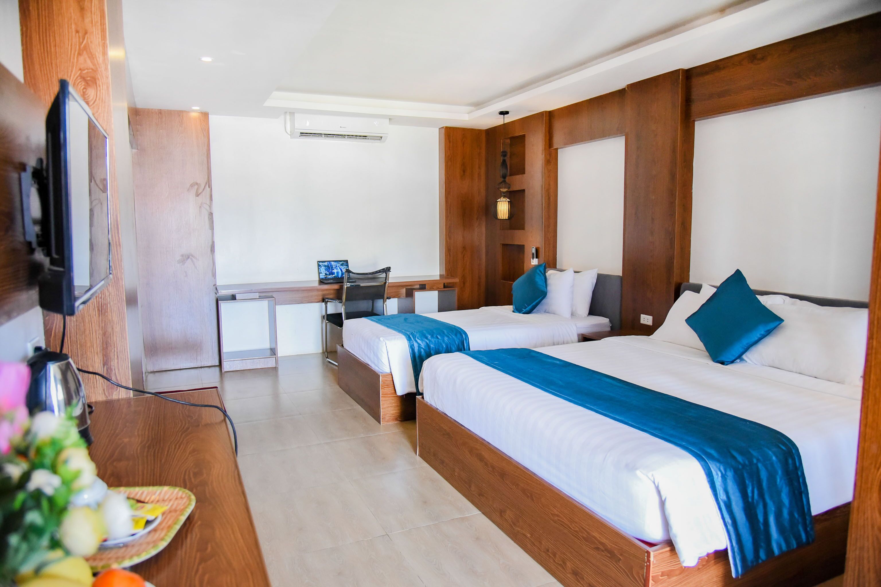 A hotel room with two beds, a desk, a chair, a TV, and a wooden wall panel.