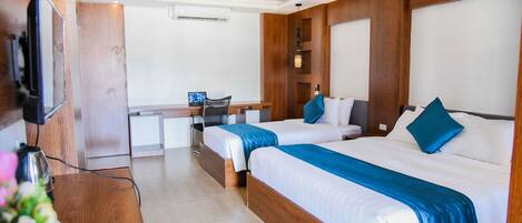 A hotel room with two beds, a desk, a chair, a TV, and a wooden wall panel.