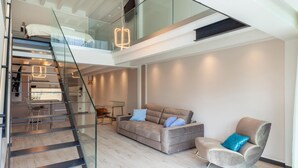 Un espace de vie moderne comprenant un escalier menant à une chambre en mezzanine, un canapé, un fauteuil et un coin repas.