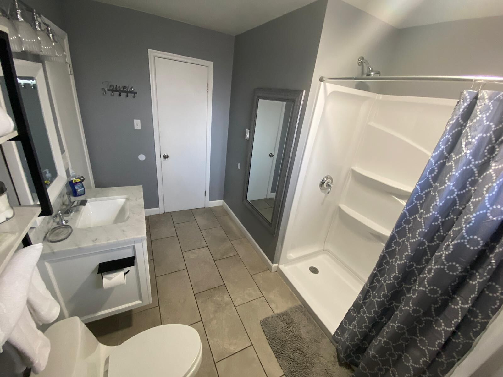 A bathroom with a white sink, mirror, and toilet. There is a shower with a patterned curtain.