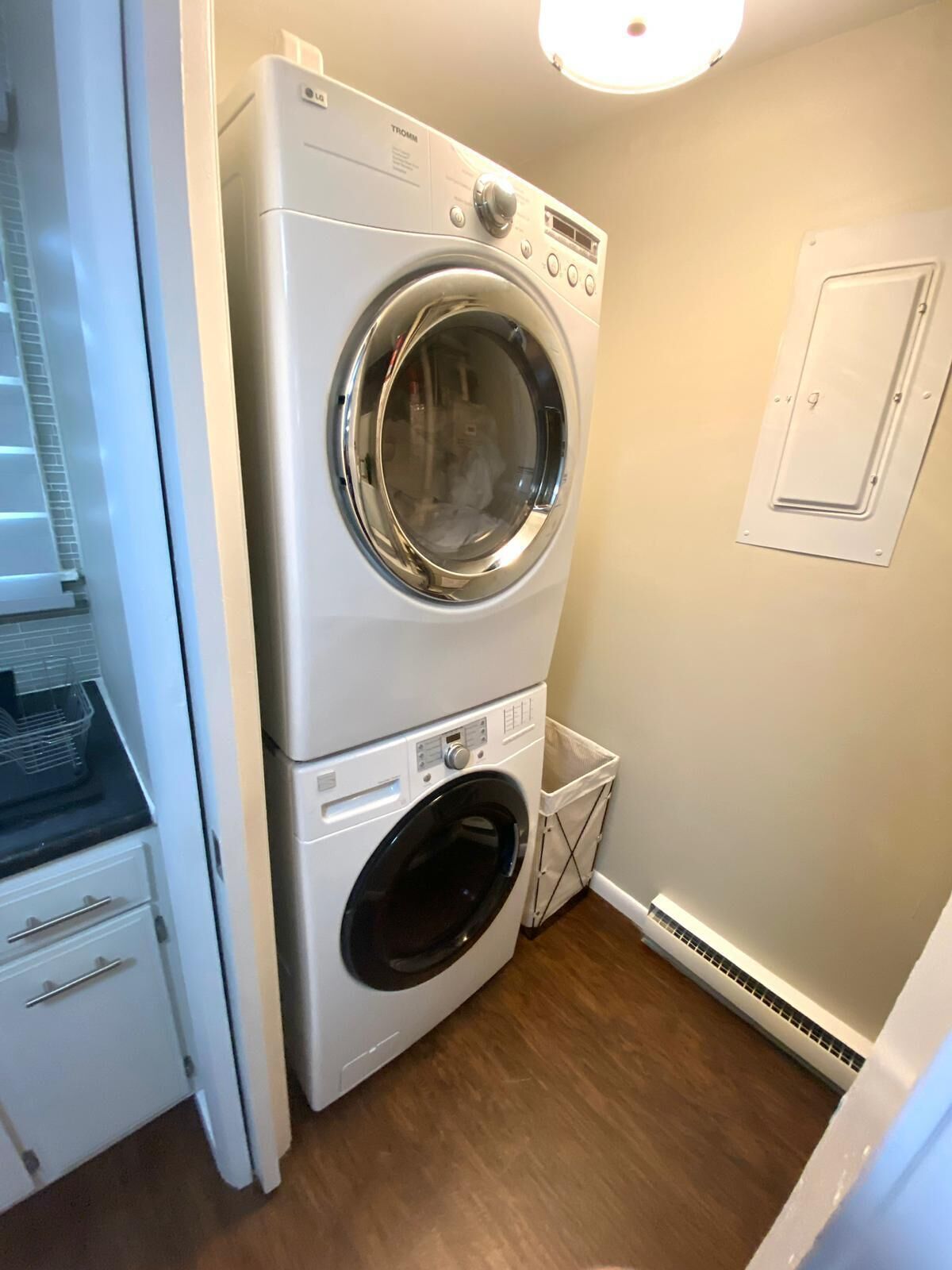 Une petite buanderie comprenant un lave-linge et un sèche-linge superposés, une petite poubelle et une porte blanche.