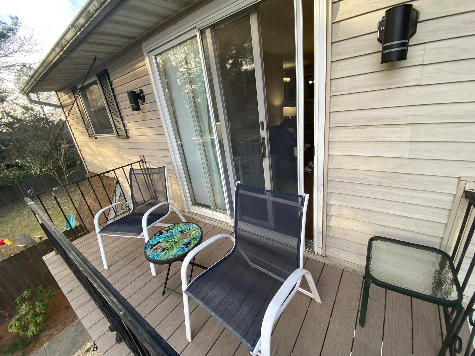 Une terrasse couverte avec deux chaises et une table, une porte-fenêtre coulissante et un petit luminaire extérieur.
