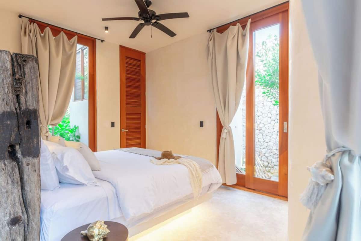 Un dormitorio con cama, ventilador de techo y vista a zonas verdes.