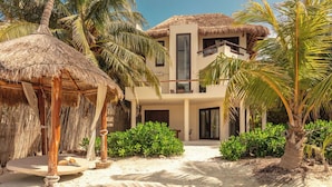 A beachfront villa with a thatched roof, a balcony, and lush tropical vegetation. - Casa Punta Coco & Beach Club (Isla Holbox)