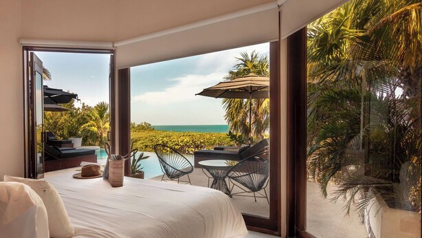 A bedroom with a large bed, a view of the ocean, and outdoor seating with umbrellas. - Casa Punta Coco & Beach Club (Isla Holbox)