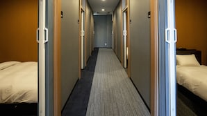 Un pasillo de hotel con dos camas a cada lado, piso alfombrado y puertas con picaporte.