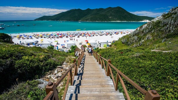 Un escalier en bois mène à une plage où sont installées des tentes et des parasols blancs.
