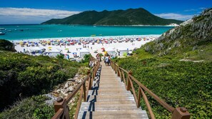 A wooden staircase leading to a beach with white tents and umbrellas. - House in Praia dos Anjos (Arraial do Cabo)