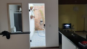 Une cuisine avec un plan de travail noir, un téléviseur et un mur en briques visible à travers une porte ouverte.