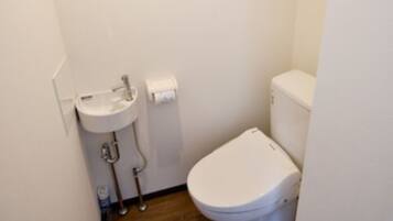 A small, compact bathroom with a white sink, toilet, and wooden flooring.
